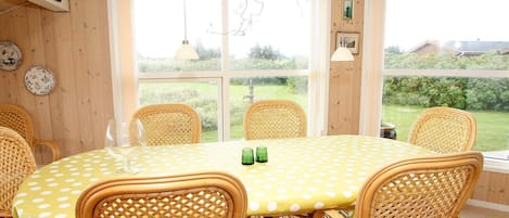 A dining area with a round table covered in a yellow polka dot tablecloth, surrounded by wicker chairs, and large windows offering a view of the outdoors.