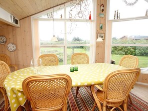 A dining area with a round table covered in a yellow polka dot tablecloth, surrounded by wicker chairs, and large windows offering a view of the outdoors.