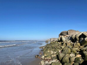 A rocky shoreline with waves, a clear sky, and a large concrete structure.