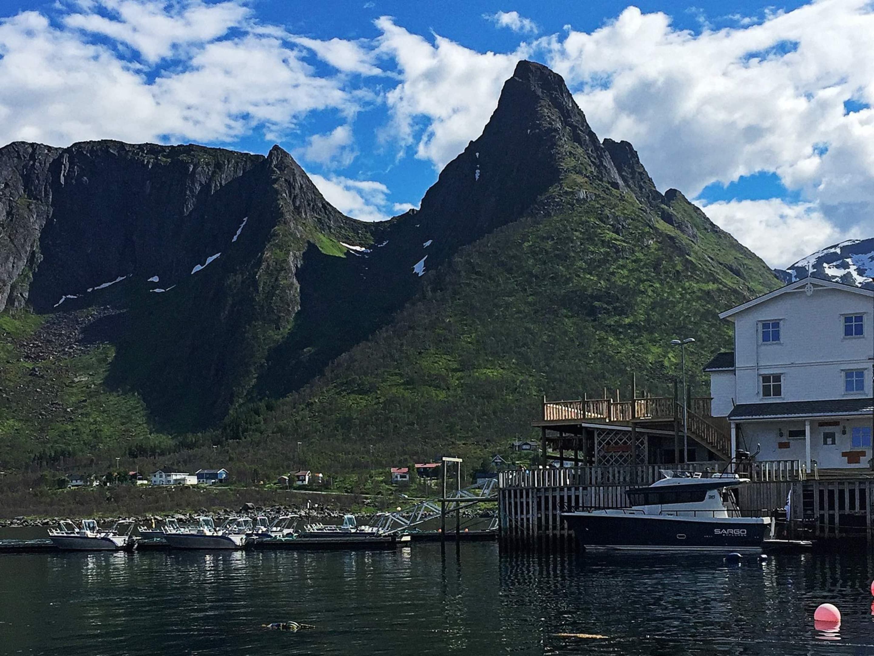Un puerto deportivo con barcos amarrados, un muelle de madera y un edificio de fachada blanca.