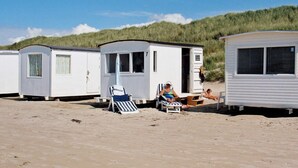 A row of mobile homes on a sandy beach with a grassy dune in the background. - 8 Person Holiday Home in Lokken (Lokken)