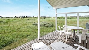 A covered outdoor area with a wooden deck, white plastic chairs, and a table. - 8 Person Holiday Home in Lokken (Lokken)
