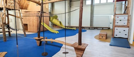 A play area with wooden climbing structures, a slide, and soft flooring.