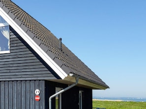 A building with a sloped roof, a visible number '21' sign, and a view of the sea in the background. - Holiday Home in Wendtorf (Wendtorf)