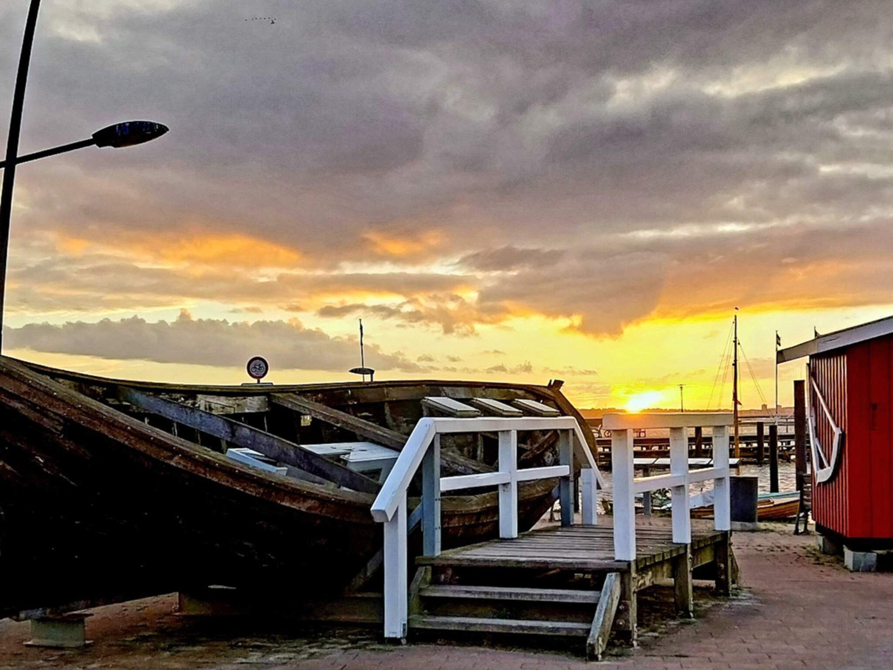 A dock with boats, a wooden walkway, and a red building.