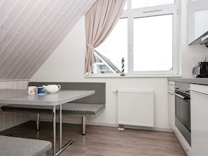 A modern kitchen with a built-in oven, a dining table with a bench, and a window with curtains. - Holiday Home in Wendtorf (Wendtorf)