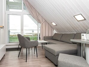 A modern loft bedroom with a large window, a gray sofa, a small table, and a chair. - Holiday Home in Wendtorf (Wendtorf)