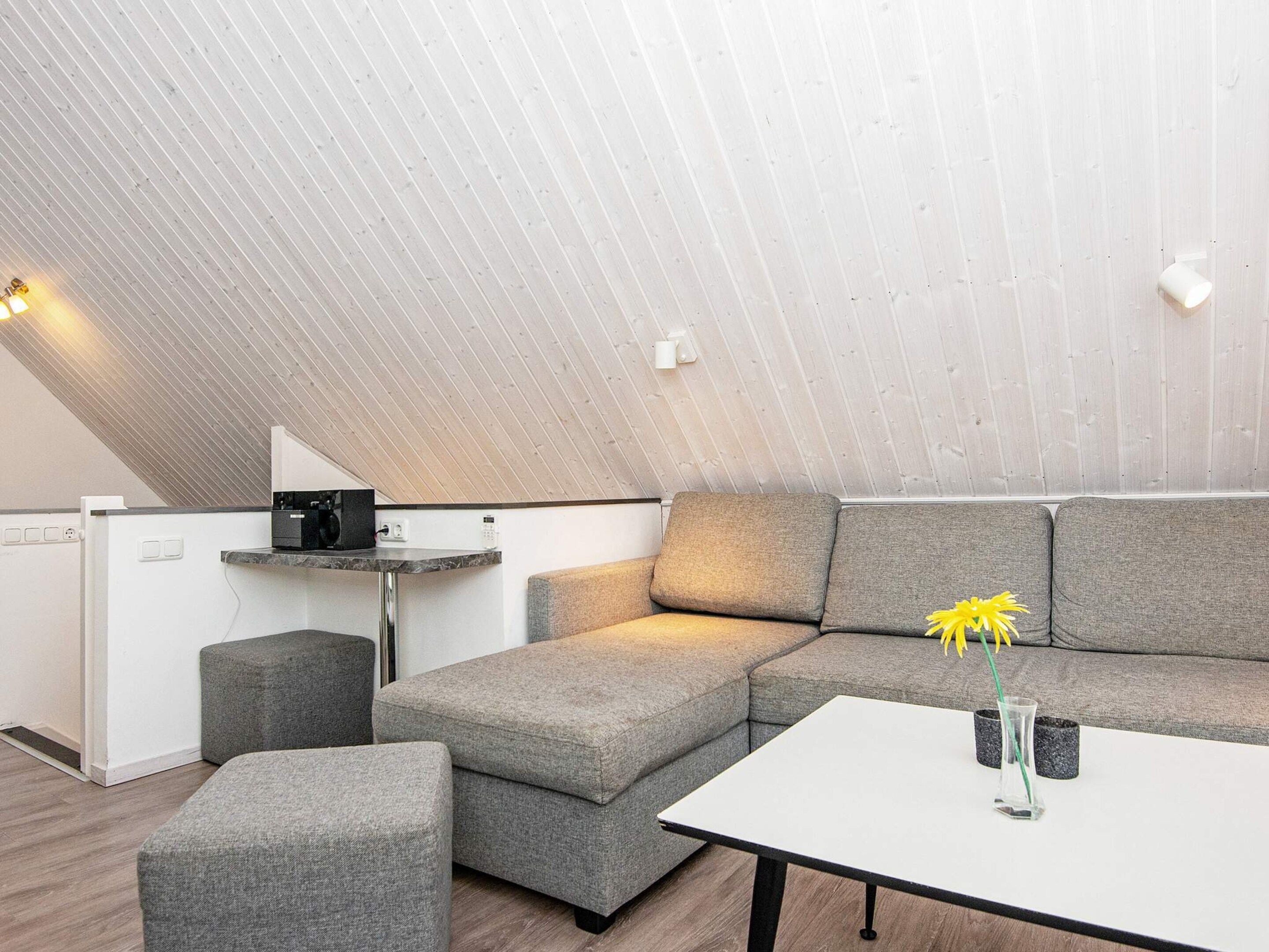 A modern loft bedroom with a sloped ceiling, a sectional sofa, a small table, and a coffee machine.