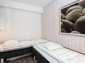 A single bed with white bedding in a room with light wooden paneling and a framed picture on the wall.