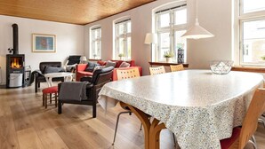 Een gezellige woonkamer met een open haard, een eethoek met een ronde tafel, en een keuken op de achtergrond.