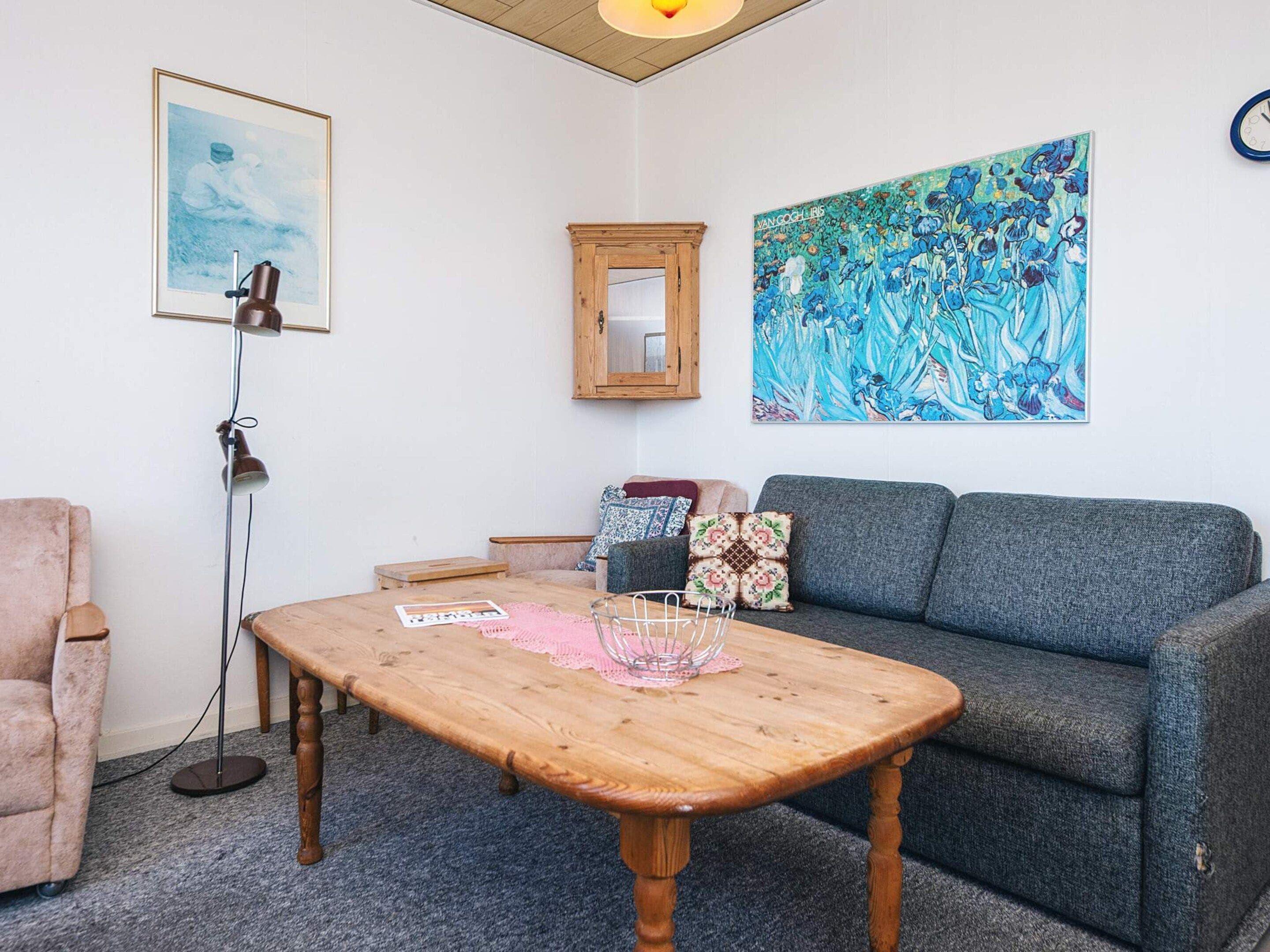 A room with a wooden table, a grey sofa, a framed painting, and a floor lamp.