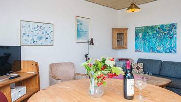 Ein gemütliches Wohnzimmer mit einem runden Holztisch, einer Couch, einem Fernseher und Kunstwerken an den Wänden.