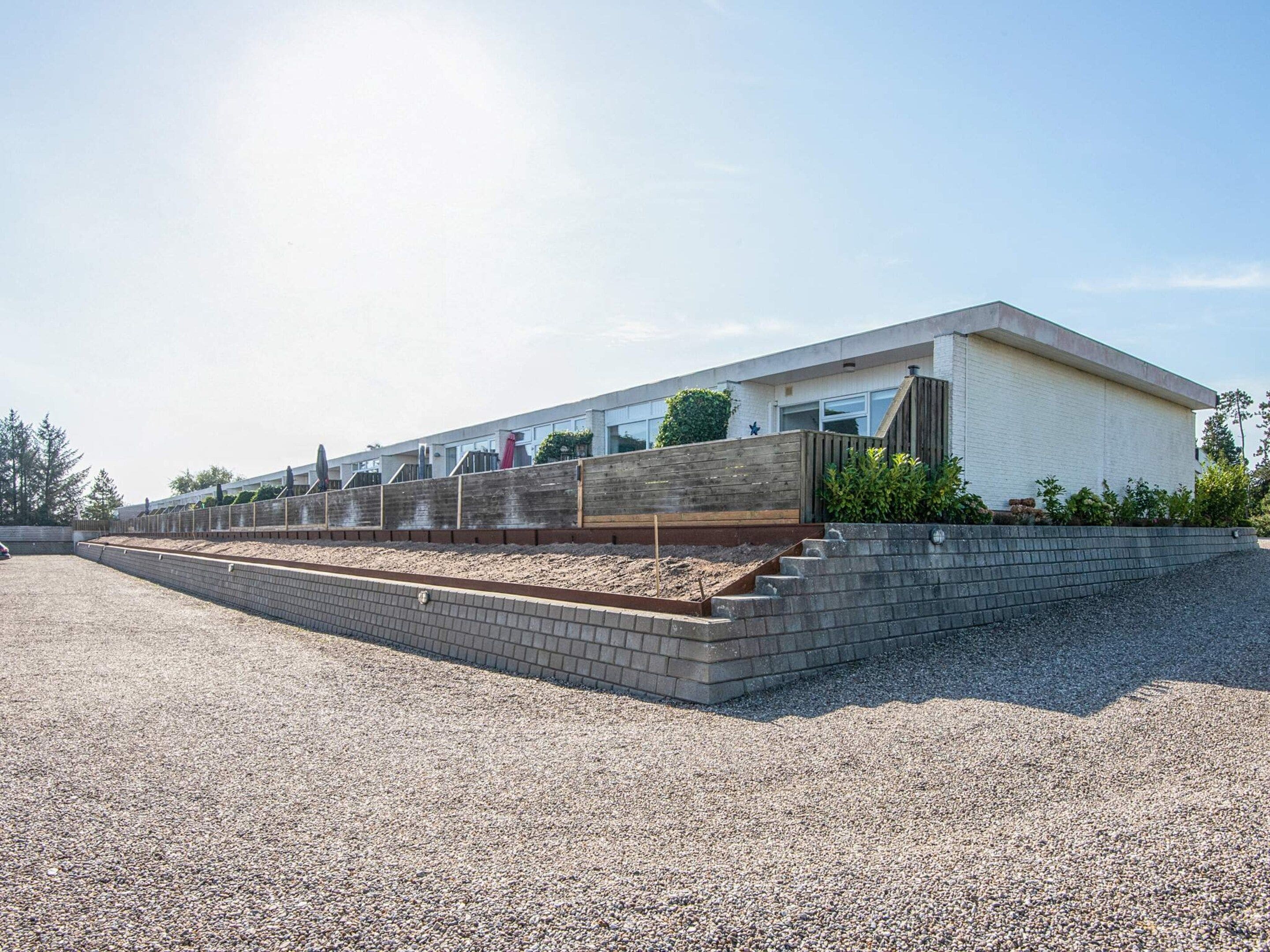 A modern building with a flat roof, a brick retaining wall, and a gravel driveway.