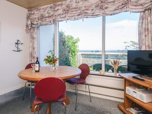 Une pièce avec une table ronde, des chaises rouges, un téléviseur et une vue sur la mer.