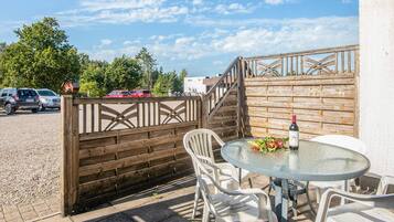 An outdoor seating area with a table and chairs, a wooden fence, and a view of parked cars and trees.