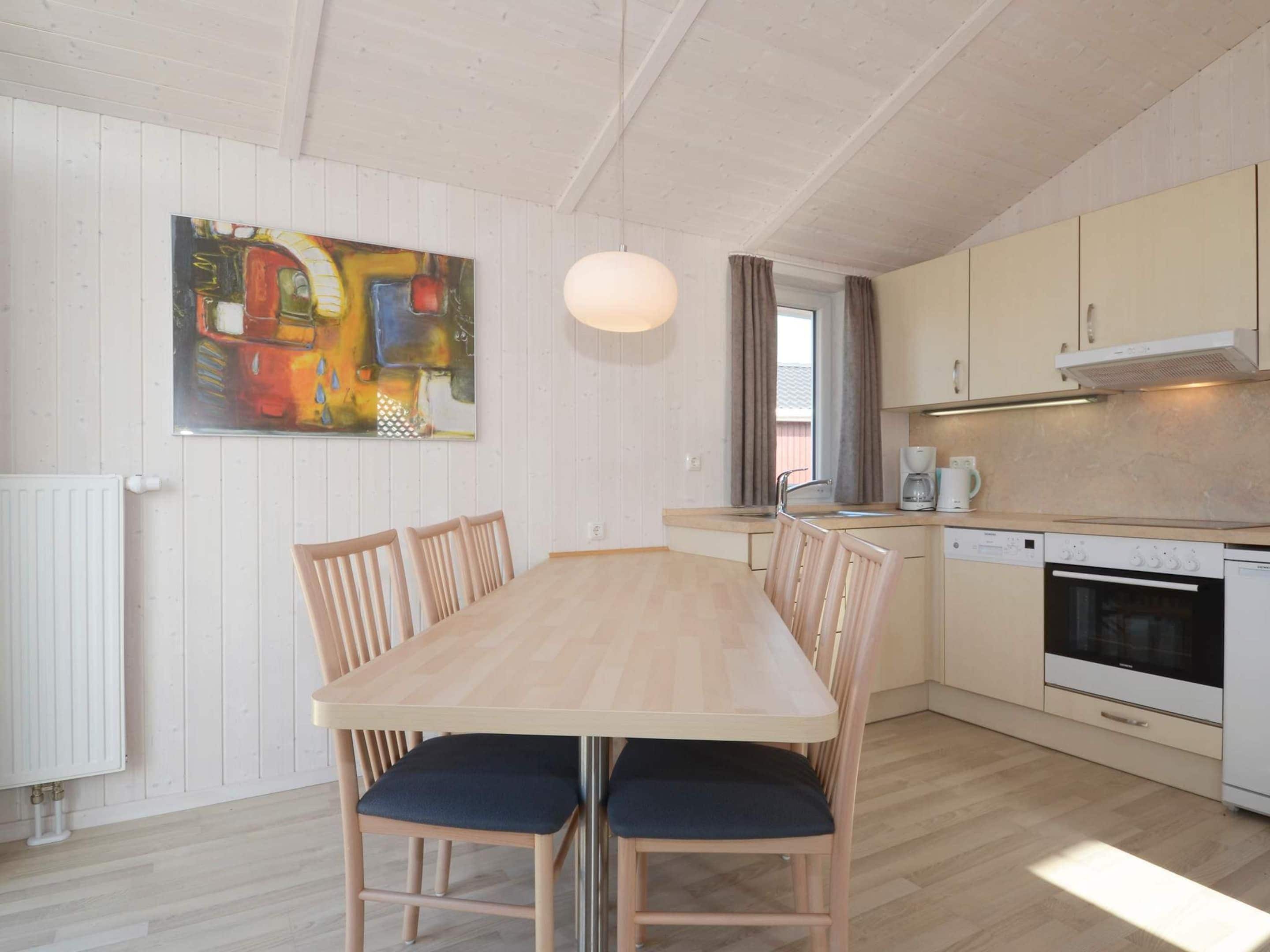 A modern kitchen with a dining table, chairs, and a painting on the wall.