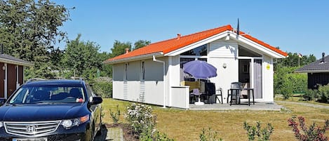 A small house with a red roof, a patio with outdoor furniture, and a car parked in front.