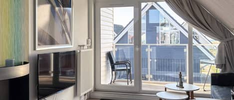 A modern living room with a TV, a sofa, a small table, and a balcony with a chair.