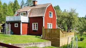 A red barn-style house with a balcony, surrounded by a wooden fence and greenery. - 4 Star Holiday Home in Sturefors (Sturefors)