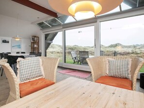 A modern room with a large glass door leading to a scenic outdoor view. Inside, there is a wooden table and wicker chairs with cushions. - Serene Holiday Home in Pandrup near Sea (Pandrup)