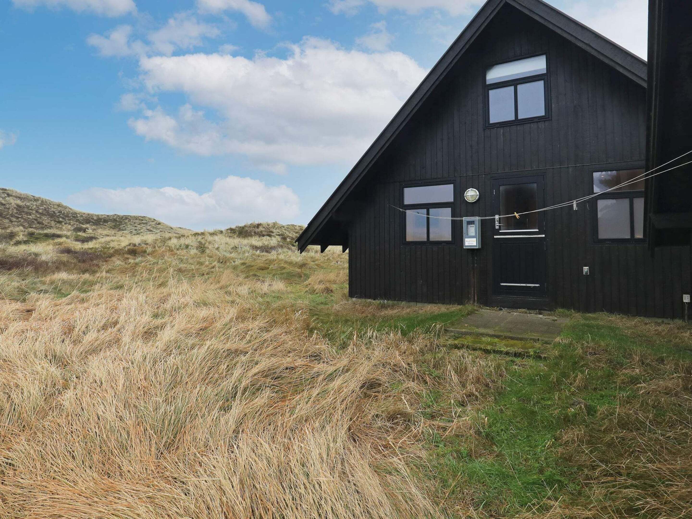 Une maison en bois noire, avec un toit en pente, un petit porche et une fenêtre ornée d’un objet circulaire sur le mur.