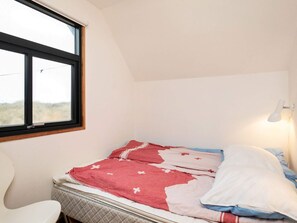 A single bed with a quilted mattress, a bedside lamp, and a window with a view of the outdoors.