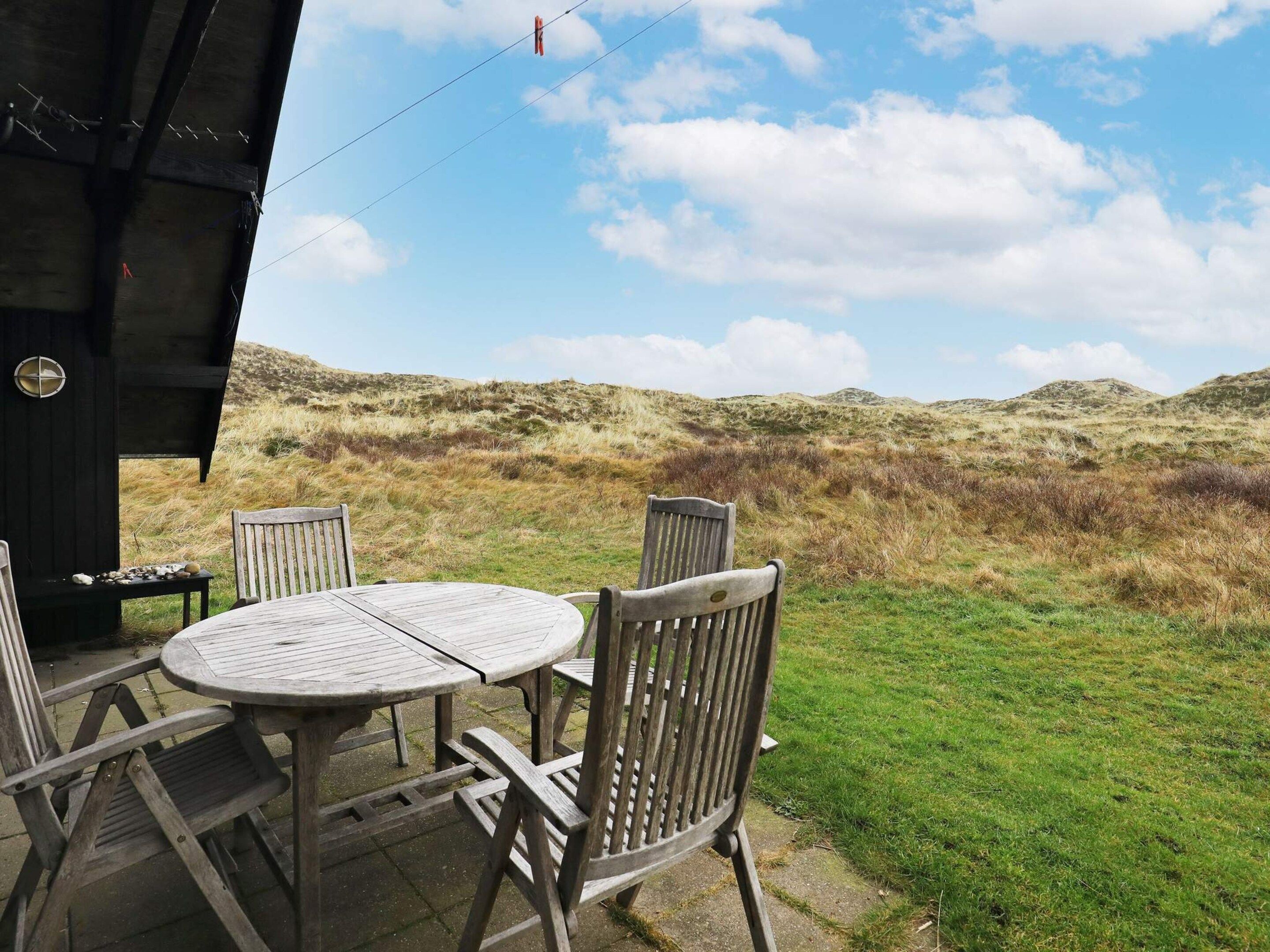 An outdoor seating area with a table and chairs, a covered structure, and a view of the surrounding landscape.