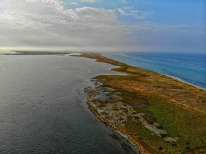 Vista aérea de un paisaje costero con una masa de agua, una franja estrecha de tierra y una carretera.