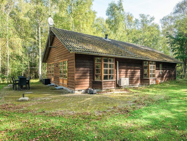 A wooden cabin with a sloped roof, a chimney, and a small porch with a table and chairs. - Cozy Holiday Home in Nordjylland near Sea (Læsø)