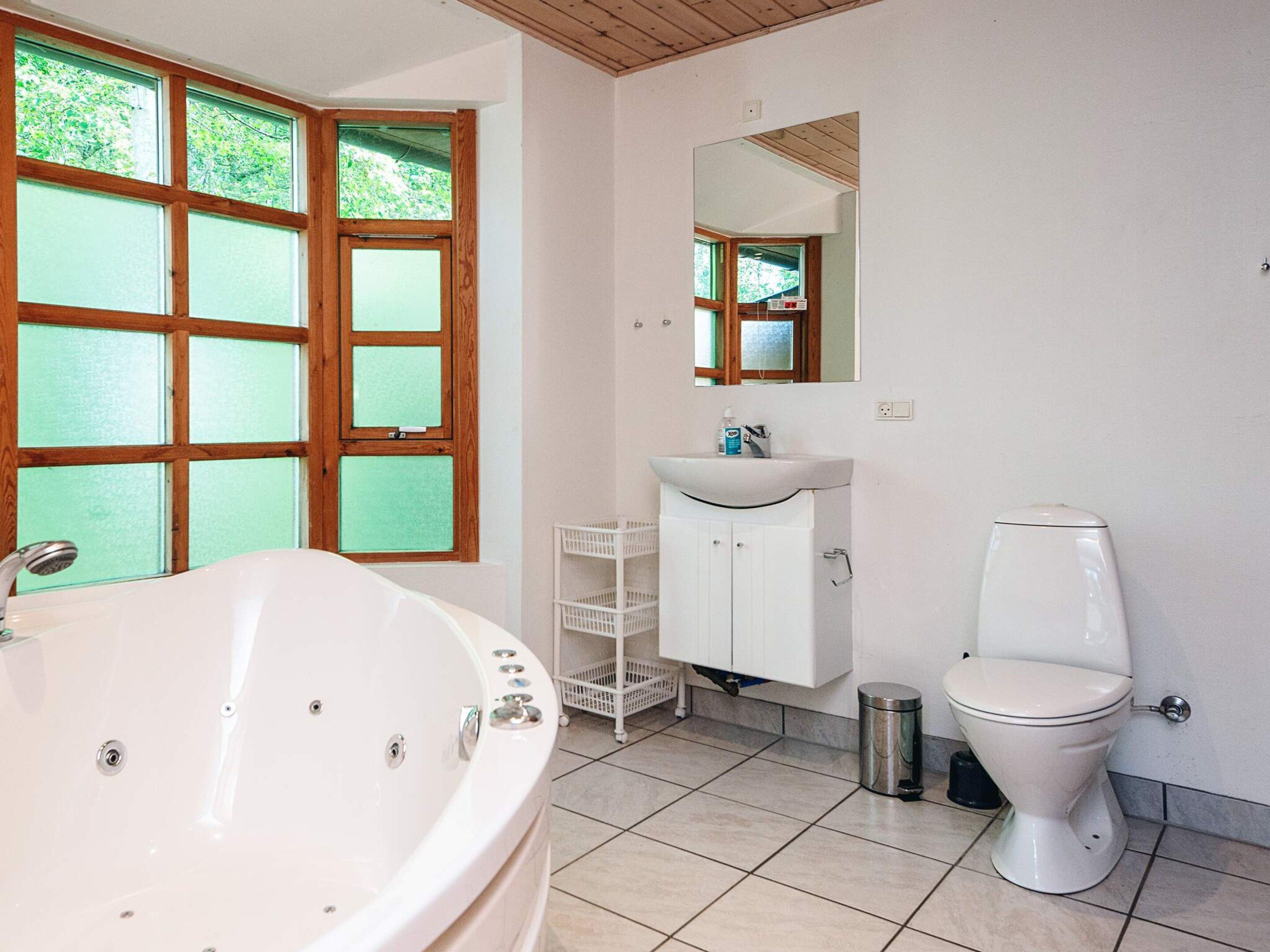 Un baño con bañera, lavabo, inodoro y ventana con vista a la vegetación.