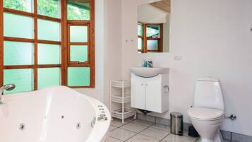Un baño con bañera, lavabo, inodoro y ventana con vista a la vegetación.