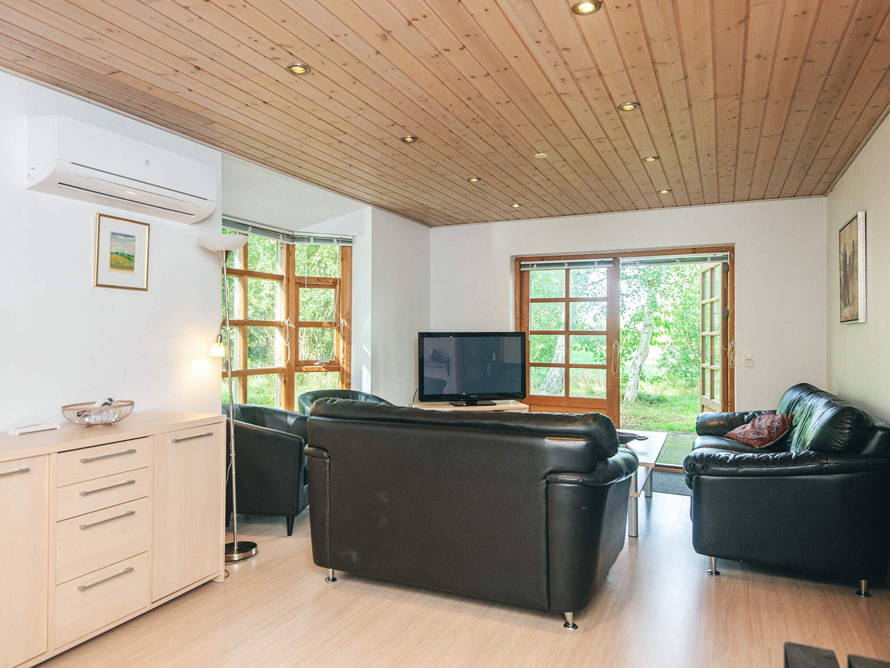 Ein Wohnzimmer mit Holzbalkendecke, einem Flachbildfernseher, einem Sofa, einem Ledersessel und einem Esstisch.