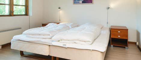 Une chambre à coucher avec un lit double, des tables de chevet, une lampe fixée au mur et une fenêtre donnant sur un paysage verdoyant.