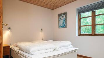 Un dormitorio con cama, lámparas de noche, una ventana con vistas a zonas verdes y un cuadro en la pared.