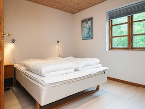 A bedroom with a bed, bedside lamps, a window with a view of greenery, and a painting on the wall. - Cozy Holiday Home in Nordjylland near Sea (Læsø)