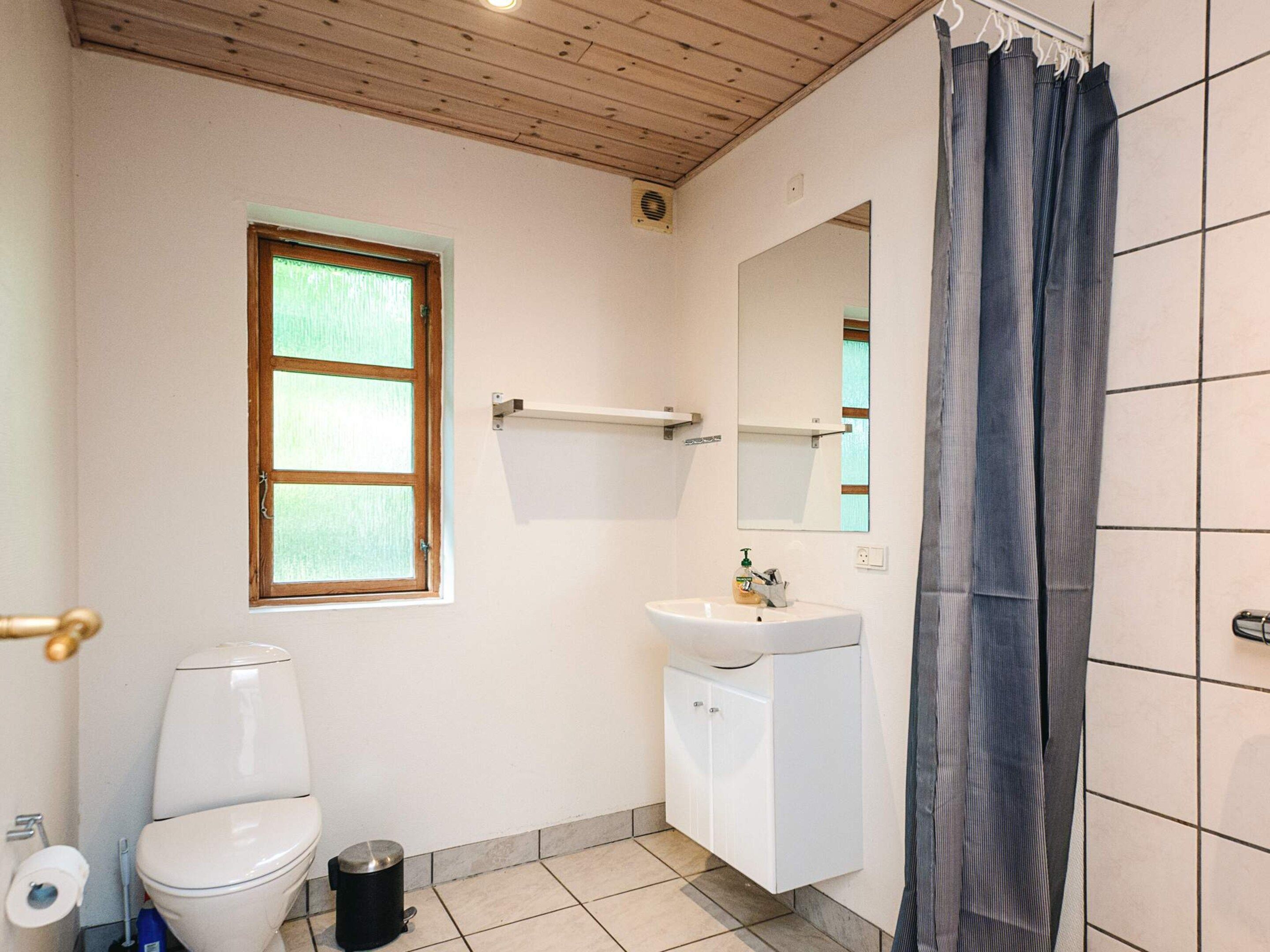 A bathroom with a toilet, sink, mirror, and a window.