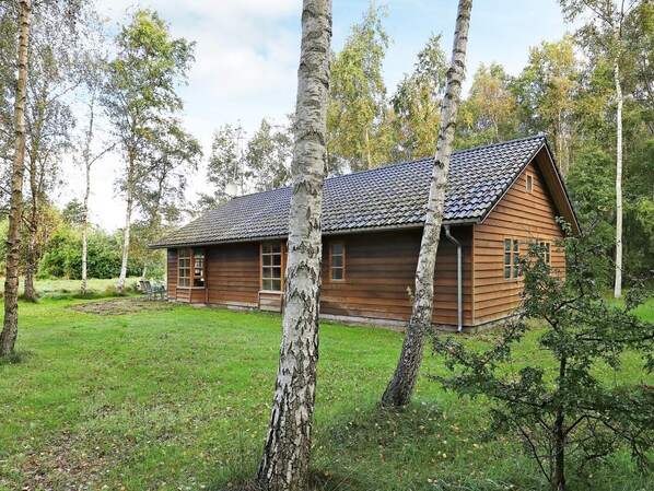 A wooden cabin with a tiled roof, surrounded by trees and a grassy area.