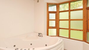 A bathroom with a freestanding bathtub, a window with wooden frames, and a white tiled floor.