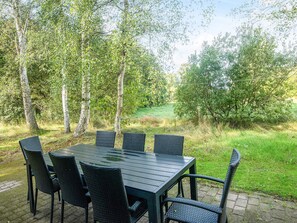 An outdoor dining area with a table and chairs, surrounded by trees and a grassy field. - Cozy Holiday Home in Nordjylland near Sea (Læsø)