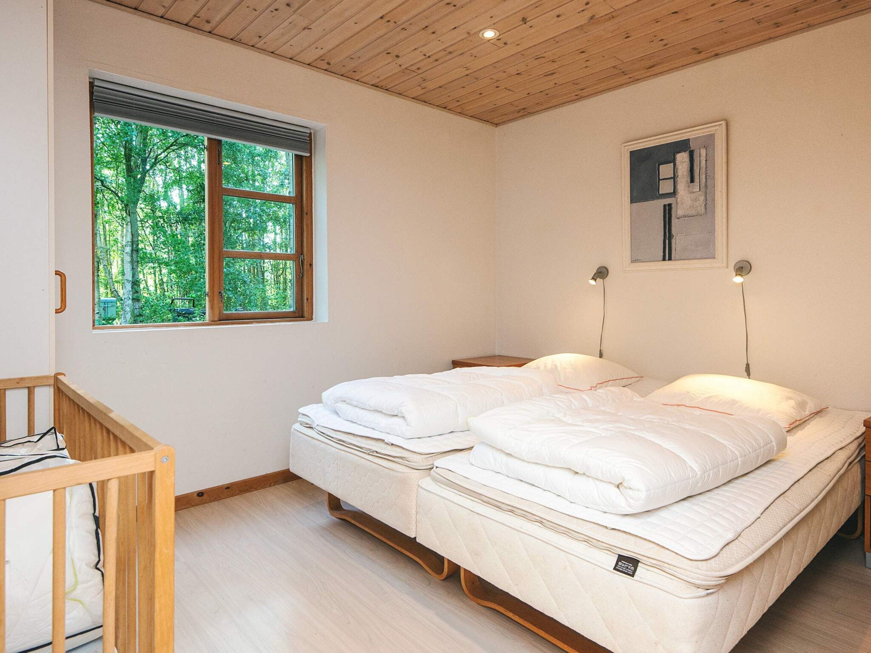 Quarto com uma cama de casal, janela com vista para árvores e um quadro na parede.