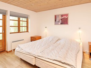 A bedroom with a bed, a nightstand, a bedside table, a window with blinds, a radiator, and a framed picture on the wall. - Cozy Holiday Home in Nordjylland near Sea (Læsø)