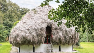 Una casa con techo de paja y un banco de madera afuera, rodeada de follaje.