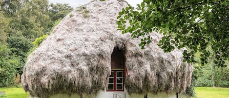 Una casa con techo de paja y un banco de madera afuera, rodeada de follaje.