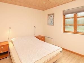 A bedroom with a bed, bedside tables, a radiator, a window with blinds, and a painting on the wall.