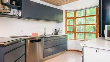 A modern kitchen with a dishwasher, a coffee maker, and a window with a view of greenery.
