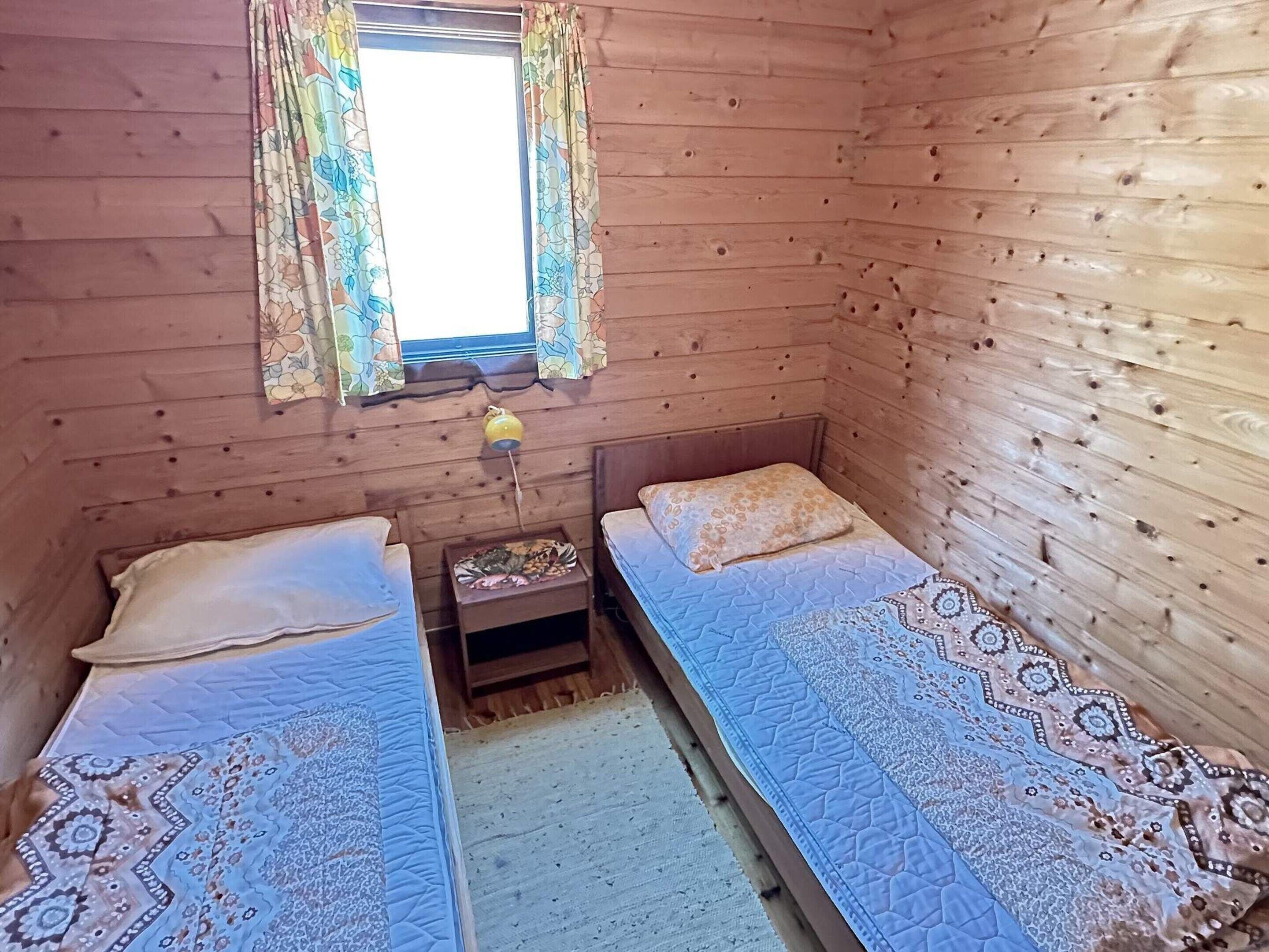 A small, wooden cabin room with two single beds, a small table, and a window with curtains.