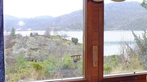A cabin with a wooden interior, a window with a view of a lake and mountains, and a table with a glass object. - 5 Person Holiday Home in Farsund (Farsund)