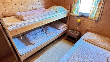 A wooden cabin room with bunk beds, a small bedside table, and a window with curtains.