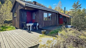 A wooden cabin with a deck, a dining area with chairs and a table, and a red door. - 5 Person Holiday Home in Farsund (Farsund)