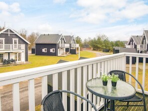 A balcony with a glass table and chairs, overlooking a row of houses with a grassy yard.